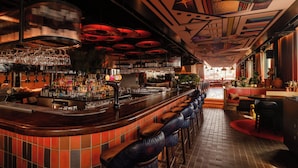 A bar area with a curved counter, multiple stools, and a variety of bottles and glasses on shelves.