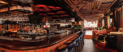A bar area with a curved counter, multiple stools, and a variety of bottles and glasses on shelves.