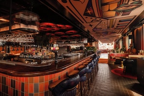 Eine Bar mit einer gebogenen Theke, mehreren Barhocker und einer Auswahl an Flaschen und Gläsern an Regalen.