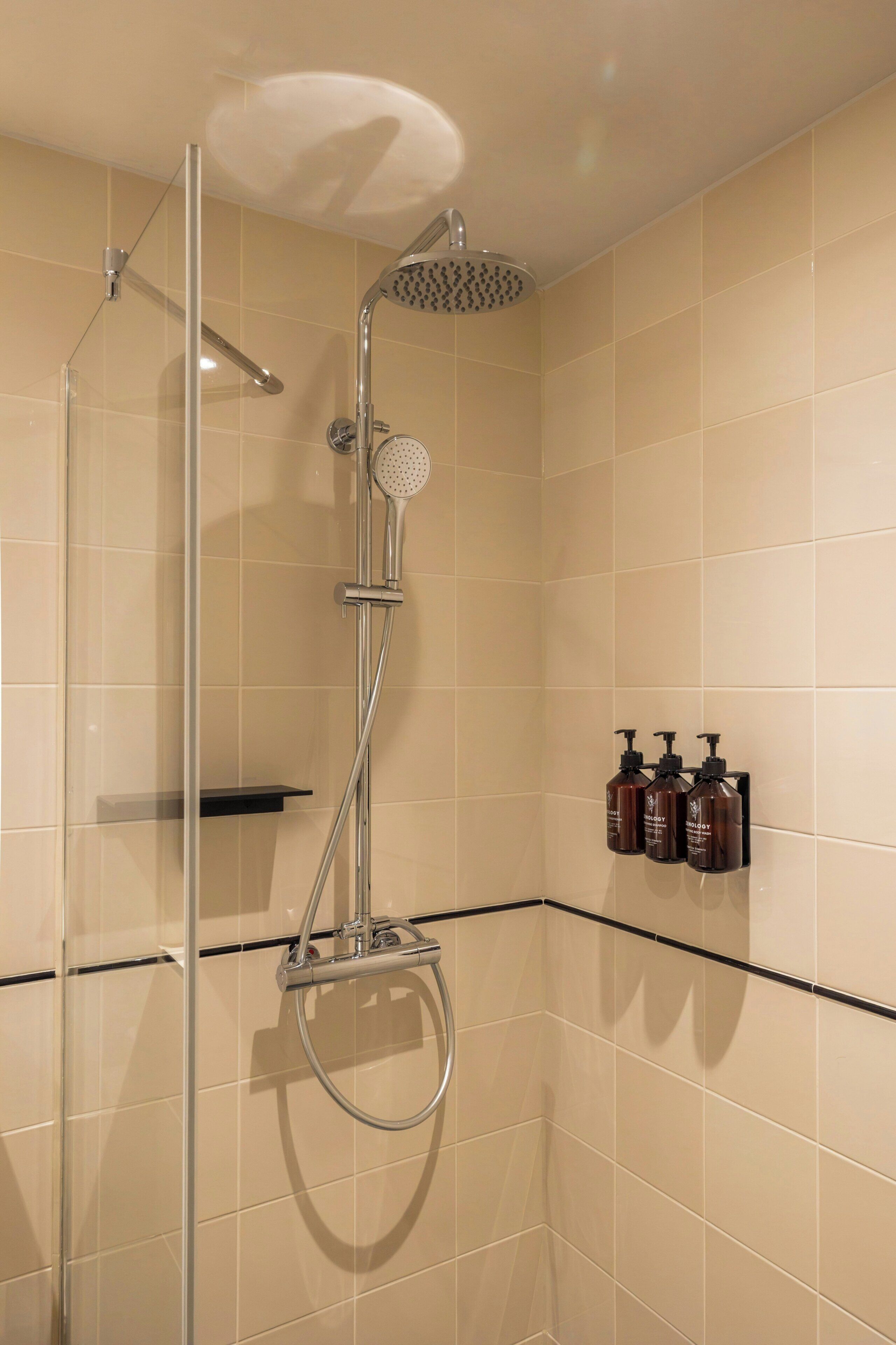 A shower with a handheld showerhead, a glass-enclosed shower, and a black shelf with toiletries.