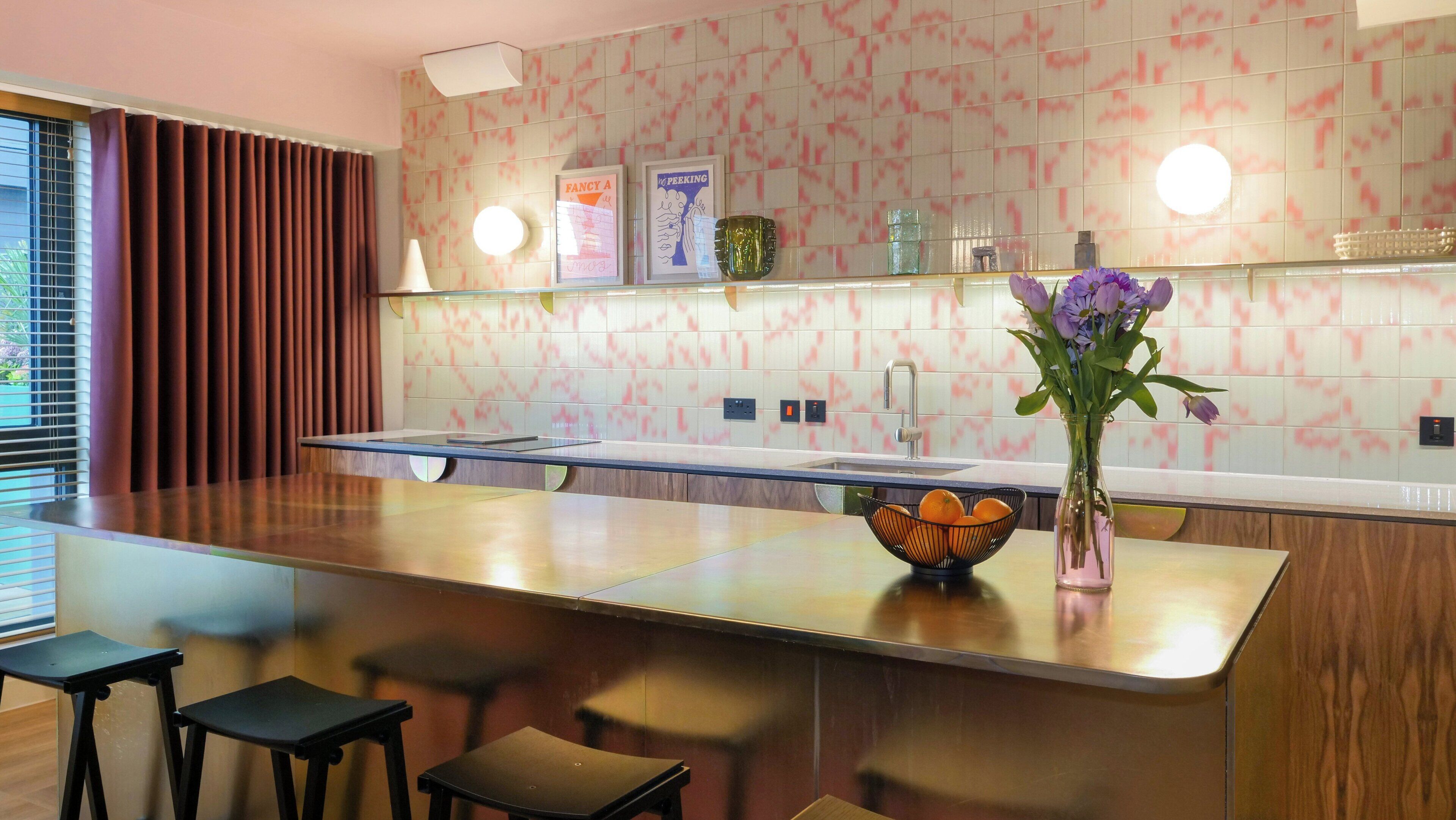 Una cocina moderna con una isla central, taburetes de bar, un jarrón con flores y un salpicadero de azulejos.