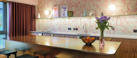 Una cocina moderna con una isla central, taburetes de bar, un jarrón con flores y un salpicadero de azulejos.