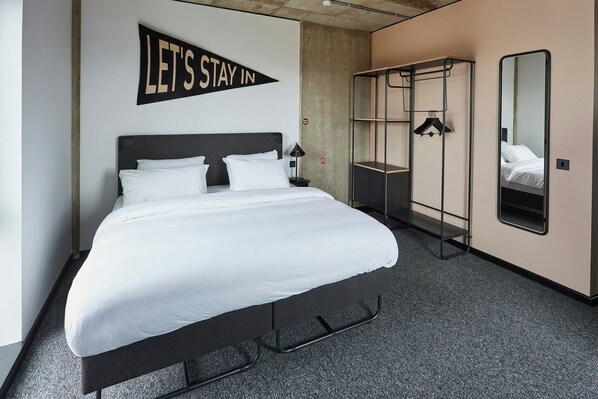 A neatly made bed with white linens, a wall-mounted sign saying 'LET'S STAY IN', a hanging coat rack, and a large mirror. - The Social Hub Glasgow (Glasgow)