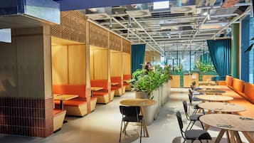 Un interior moderno con zonas de estar, mesas y una planta grande.