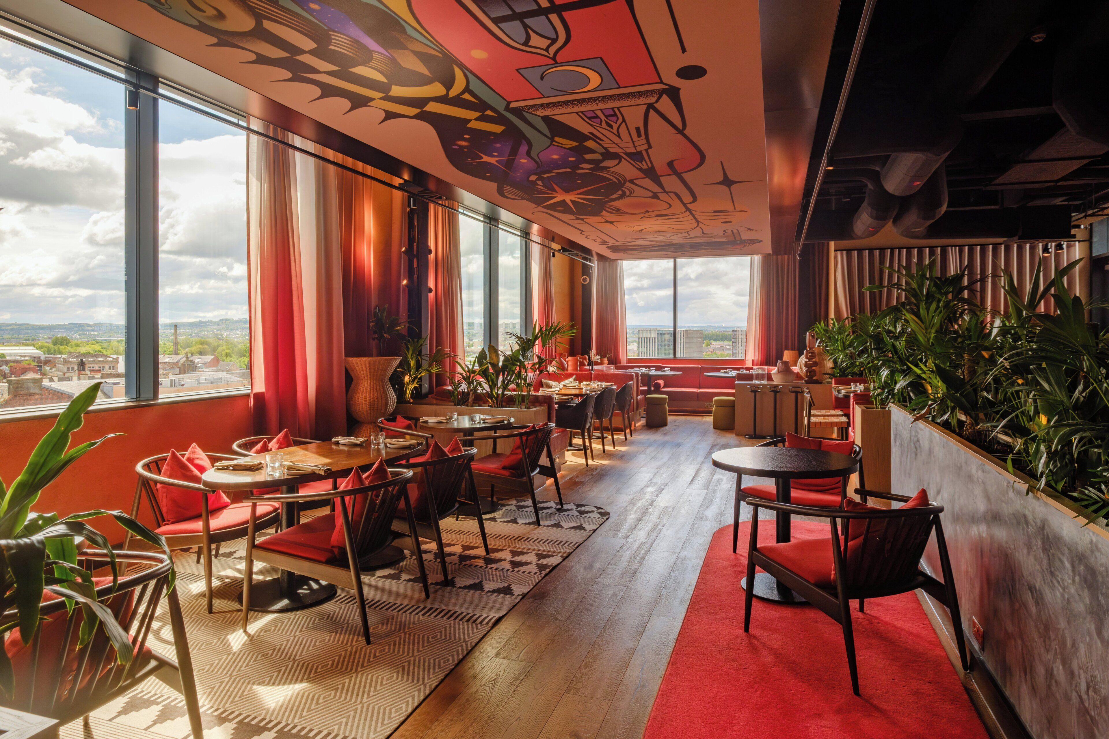 A modern interior with large windows, red seating, and indoor plants.