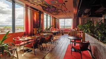 A modern interior with large windows, red seating, and indoor plants.