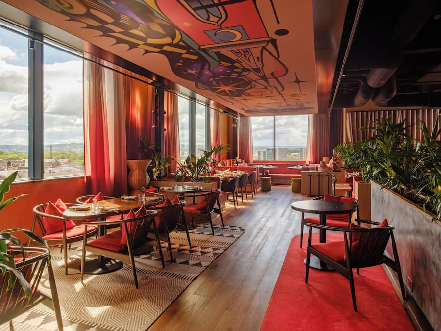 A modern interior with large windows, red seating, and indoor plants.