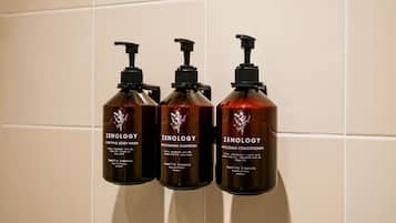 Tres botellas de Zenology con jabón líquido, champú y acondicionador sobre una pared de azulejos.