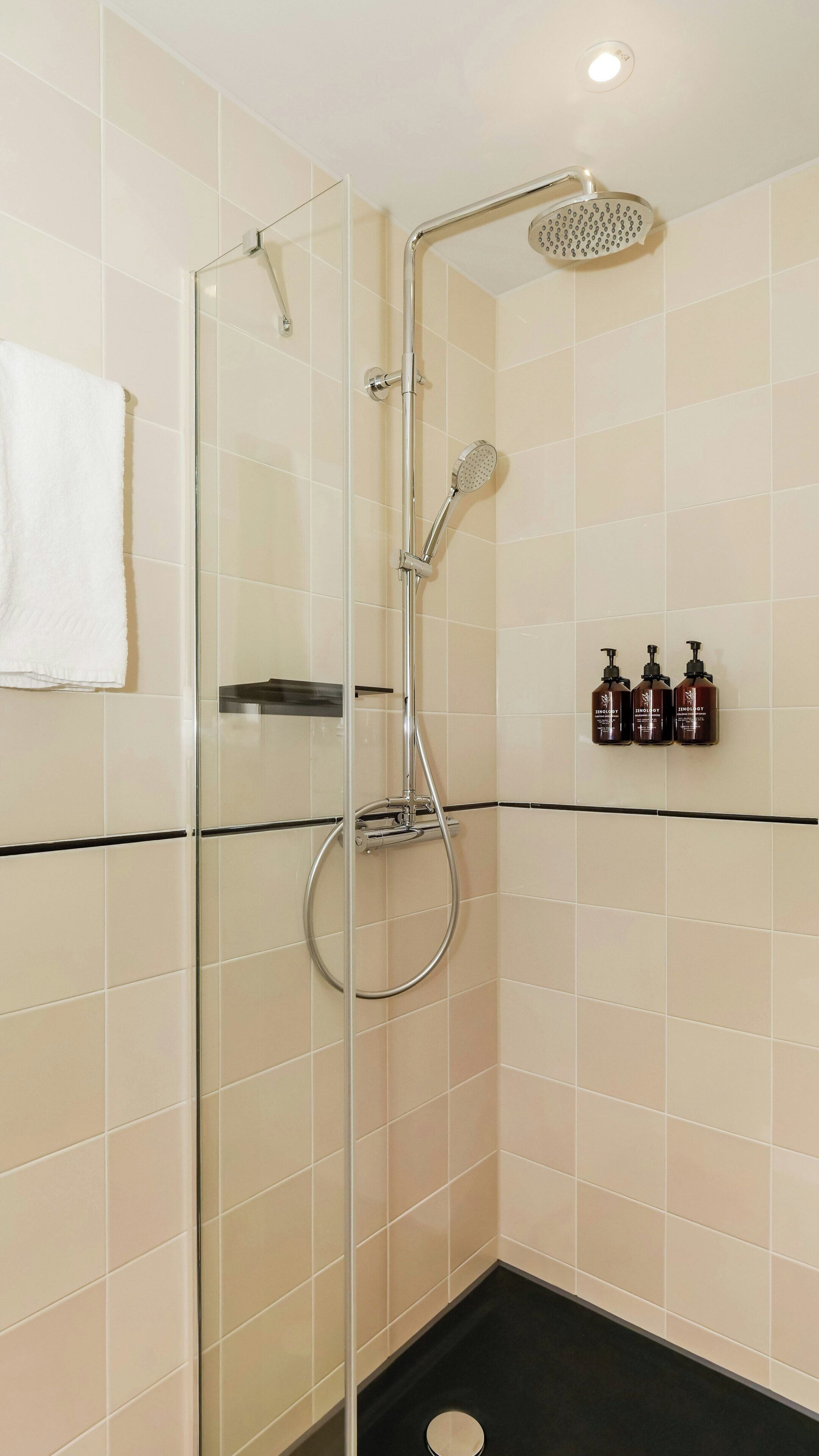 A glass-enclosed shower with a handheld showerhead, a wall-mounted faucet, and a black floor.