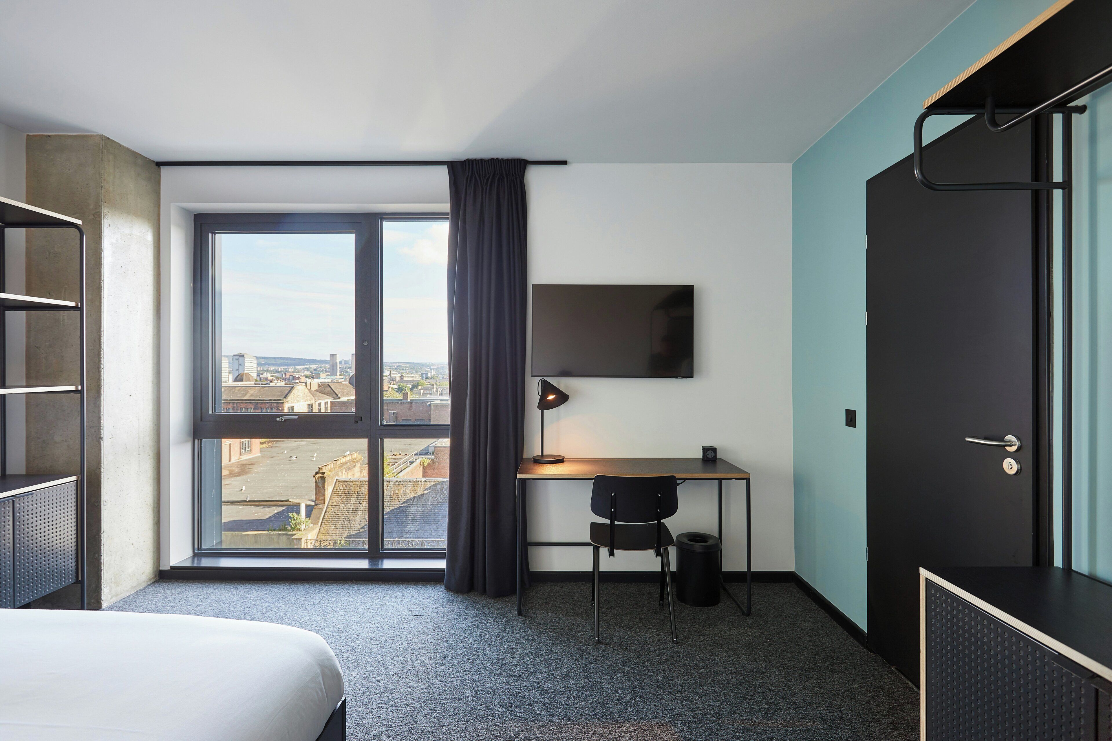 Una habitación de hotel con cama, escritorio, silla, televisor y una ventana grande con cortinas.