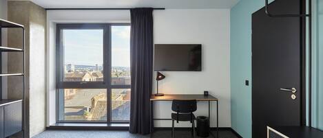 Una habitación de hotel con cama, escritorio, silla, televisor y una ventana grande con cortinas.