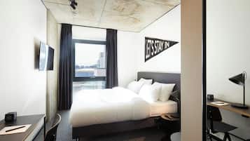 A hotel room with a bed, desk, chair, and a view of the city.
