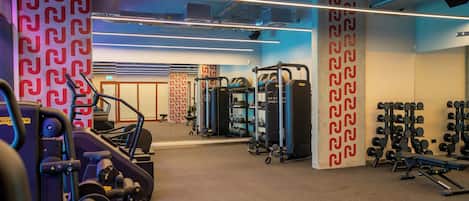 Une salle de sport équipée de machines d’exercice, de supports pour les poids et dont les murs sont décorés de motifs.