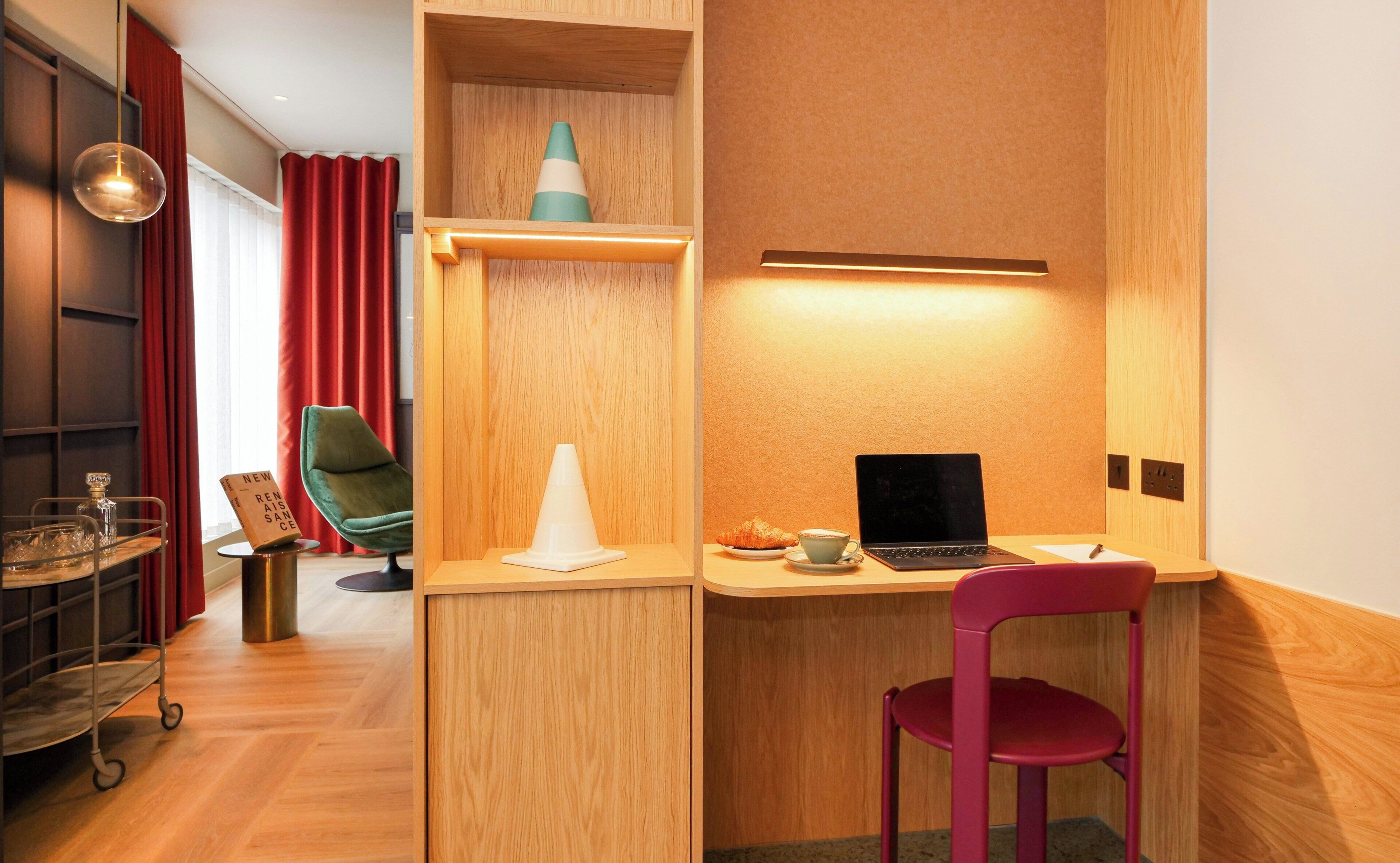 A compact workspace with a laptop, a red chair, and a small table with a croissant and a cup.