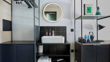 Un baño moderno con un lavamanos blanco, un espejo redondo y un perchero para toallas.