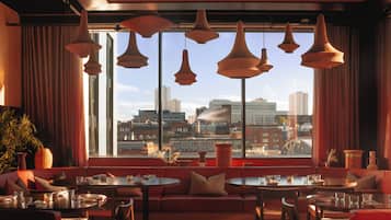 Een modern interieur met stadszicht, met een rode bank, ronde tafels en hangende pendelverlichting.