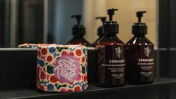 A bathroom with a mirror, a colorful soap dispenser, and two bottles of Zenolgi hair care products.