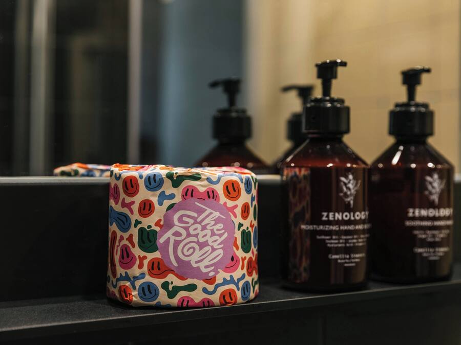A bathroom with a mirror, a colorful soap dispenser, and two bottles of Zenolgi hair care products.