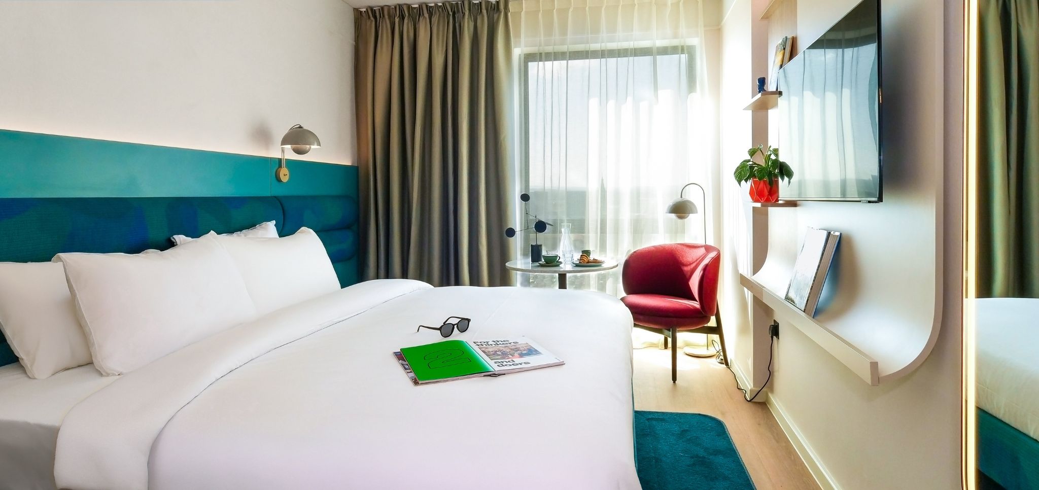 A hotel room with a bed, a desk, a chair, a TV, and a window with curtains.