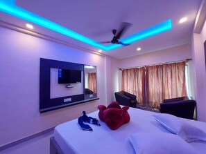 Une chambre d’hôtel avec un lit, un téléviseur fixé au mur, un ventilateur de plafond et une fenêtre avec des rideaux.