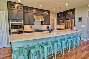 A kitchen with dark cabinets, stainless steel appliances, a central island with bar stools, and a large window.