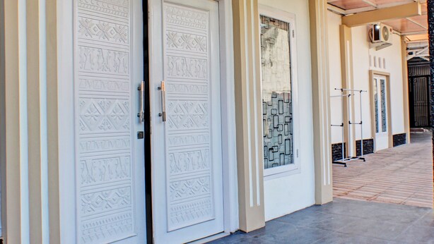 Un pasillo con dos puertas blancas decoradas con intrincados diseños, suelo de baldosas y un equipo de aire acondicionado instalado en la pared.