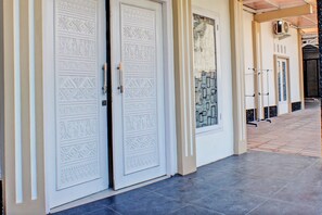 Un pasillo con dos puertas blancas decoradas con intrincados diseños, suelo de baldosas y un equipo de aire acondicionado instalado en la pared.