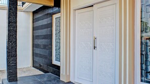 Un pasillo con piso de baldosas oscuras, un pilar texturizado y una puerta con diseños intrincados.