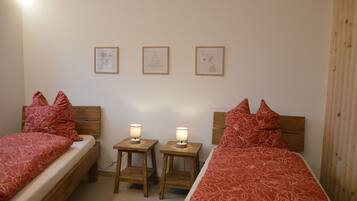 Une chambre à coucher avec deux lits simples, chacun doté d’une tête de lit en bois, d’une table de chevet avec une lampe et d’un tableau accroché au mur.
