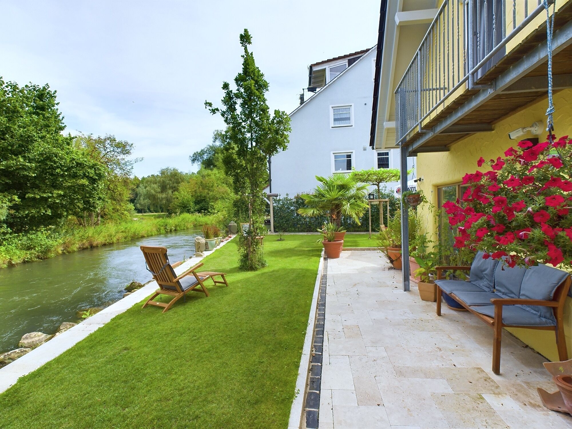 A patio with a river view, a wooden chair, and a potted plant.