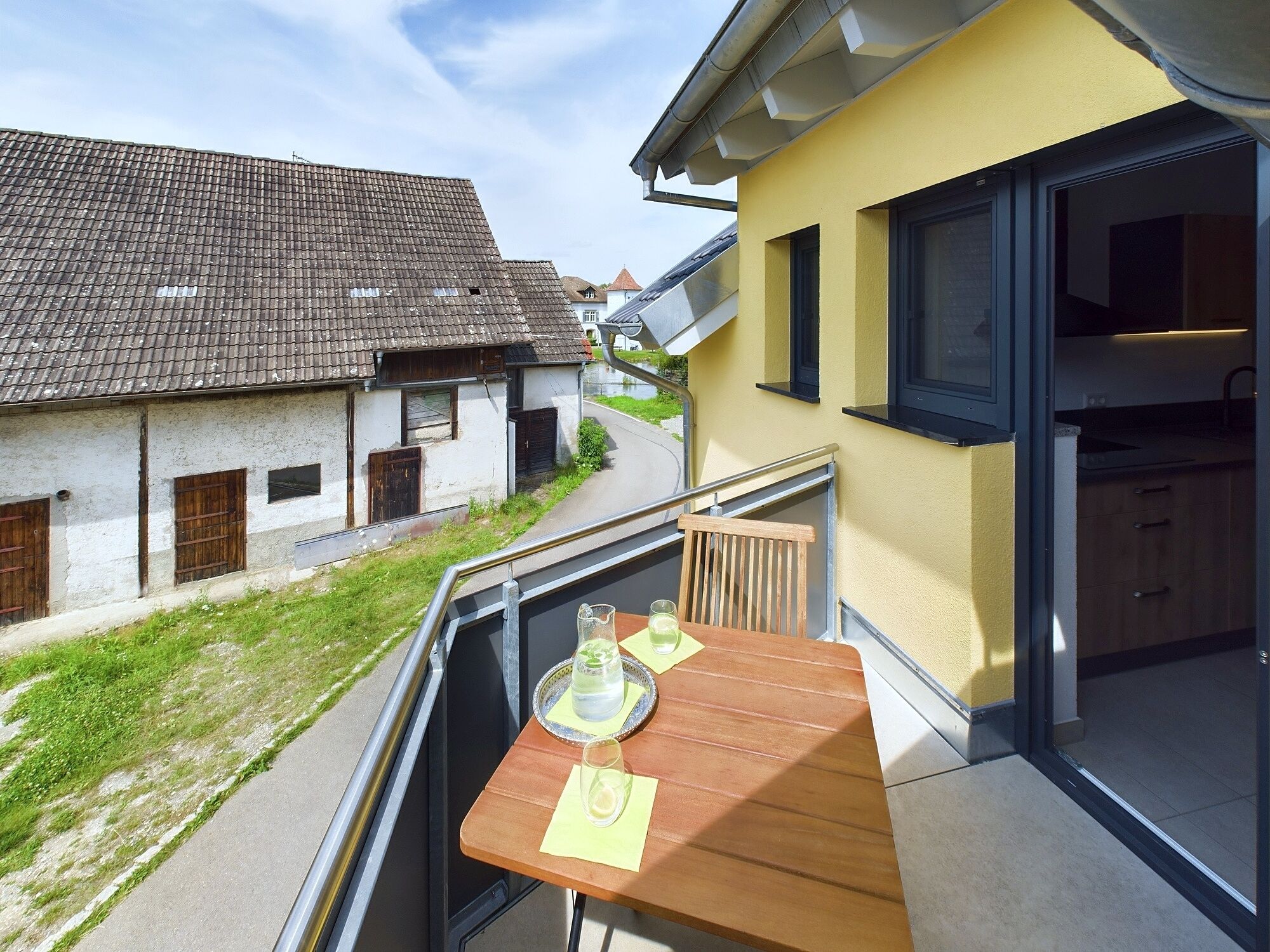 Un balcon avec une table en bois, un verre d’eau et un verre de vin.