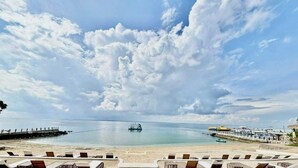 A beachside view with lounge chairs, a pier, and a calm sea under a partly cloudy sky. - Condo by the Beach OMP Mactan Int'l Airport, 2 bedrooms/2 baths sleeps 7 guests (Lapu-Lapu City)