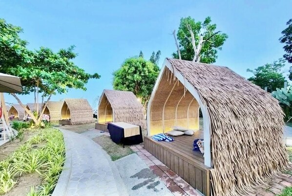 A row of thatched-roof cottages with outdoor seating areas and a paved pathway.