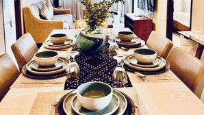 A dining area with a long table set for six, surrounded by chairs. A large vase with greenery is placed at the center. - Condo by the Beach OMP Mactan Int'l Airport, 2 bedrooms/2 baths sleeps 7 guests (Lapu-Lapu City)