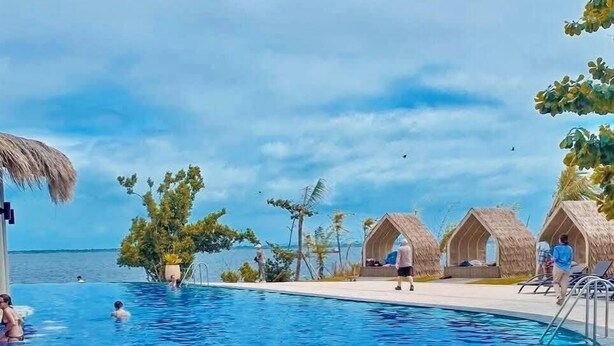 A swimming pool with clear blue water, surrounded by thatched-roof huts and palm trees. - Condo by the Beach OMP Mactan Int'l Airport, 2 bedrooms/2 baths sleeps 7 guests (Lapu-Lapu City)