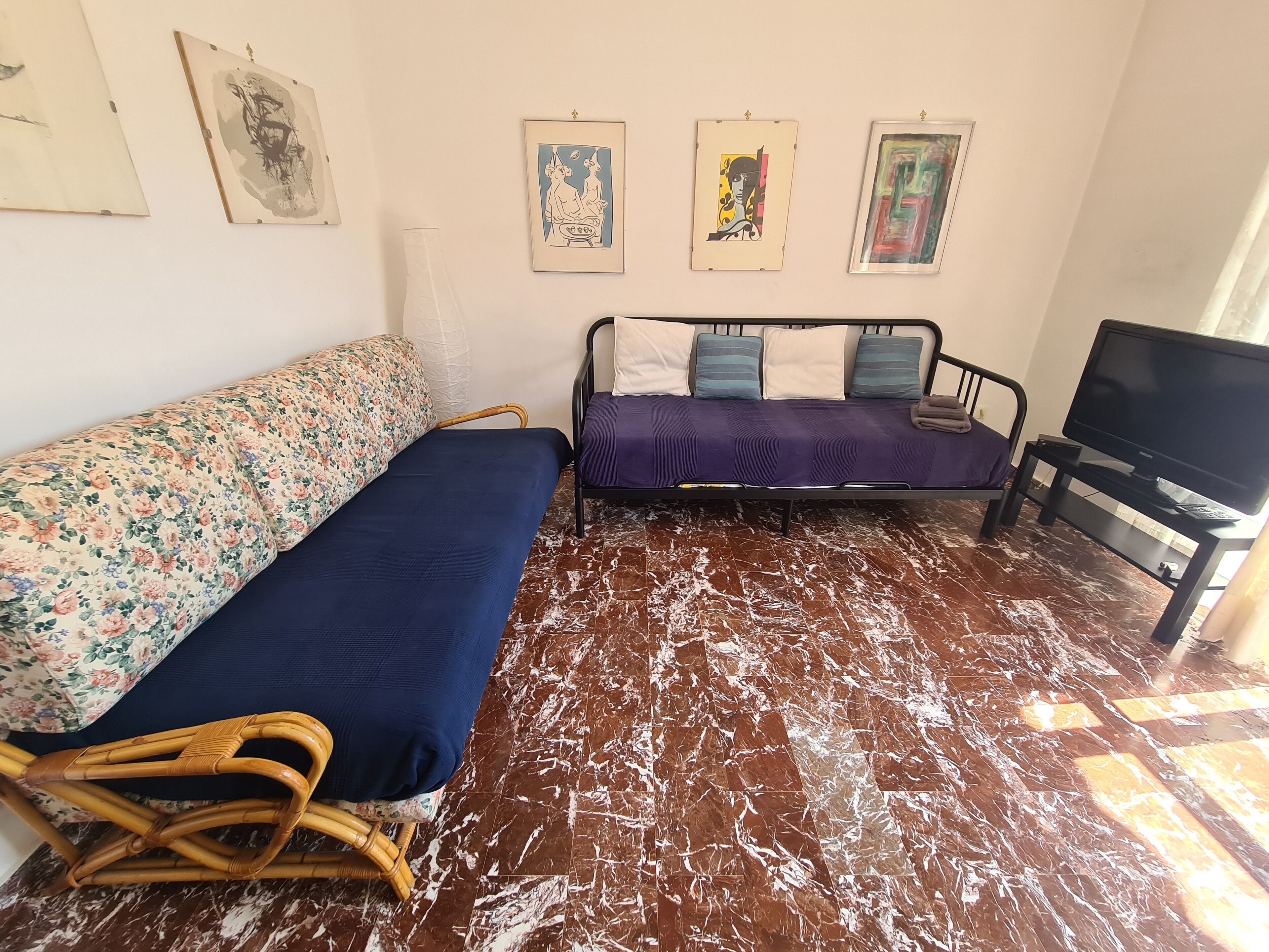 A room with two sofas, one floral and one plain, a television, and three framed artworks on the wall.