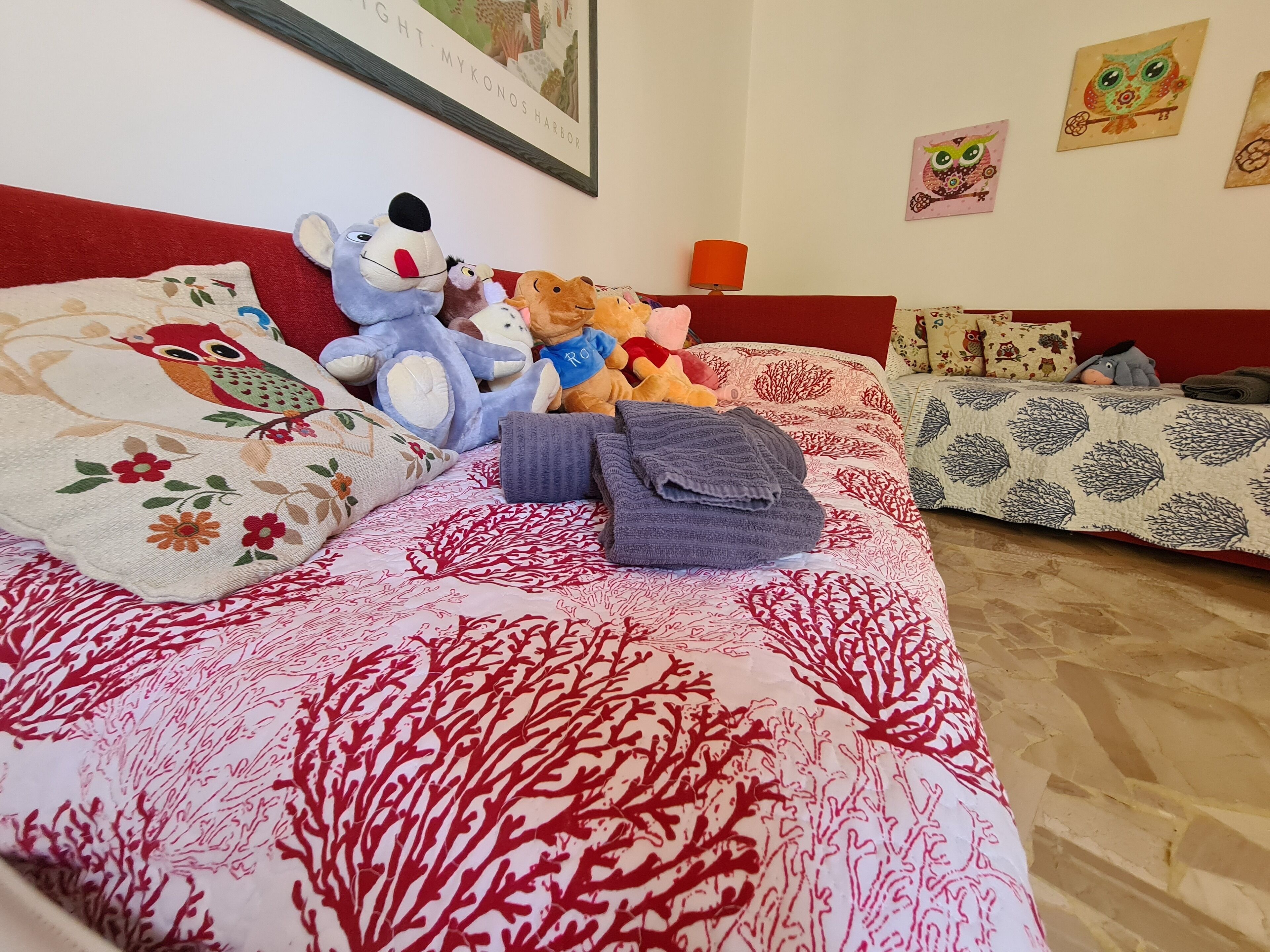 Une chambre à coucher avec un lit recouvert d’une couvre-lit à motifs rouges et blancs, une tête de lit rouge et un mur orné de tableaux encadrés.