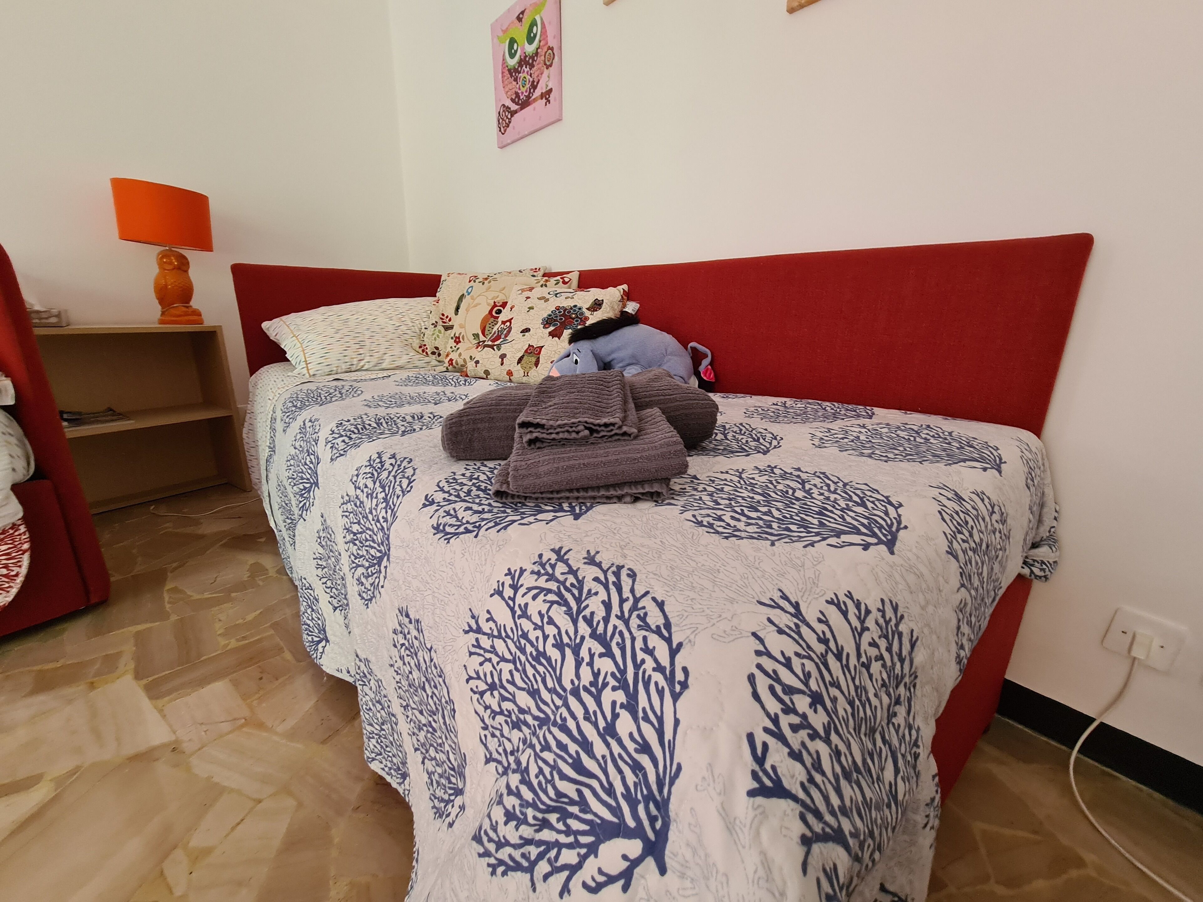 A neatly made bed with a red headboard, a patterned bedspread, and a decorative pillow.