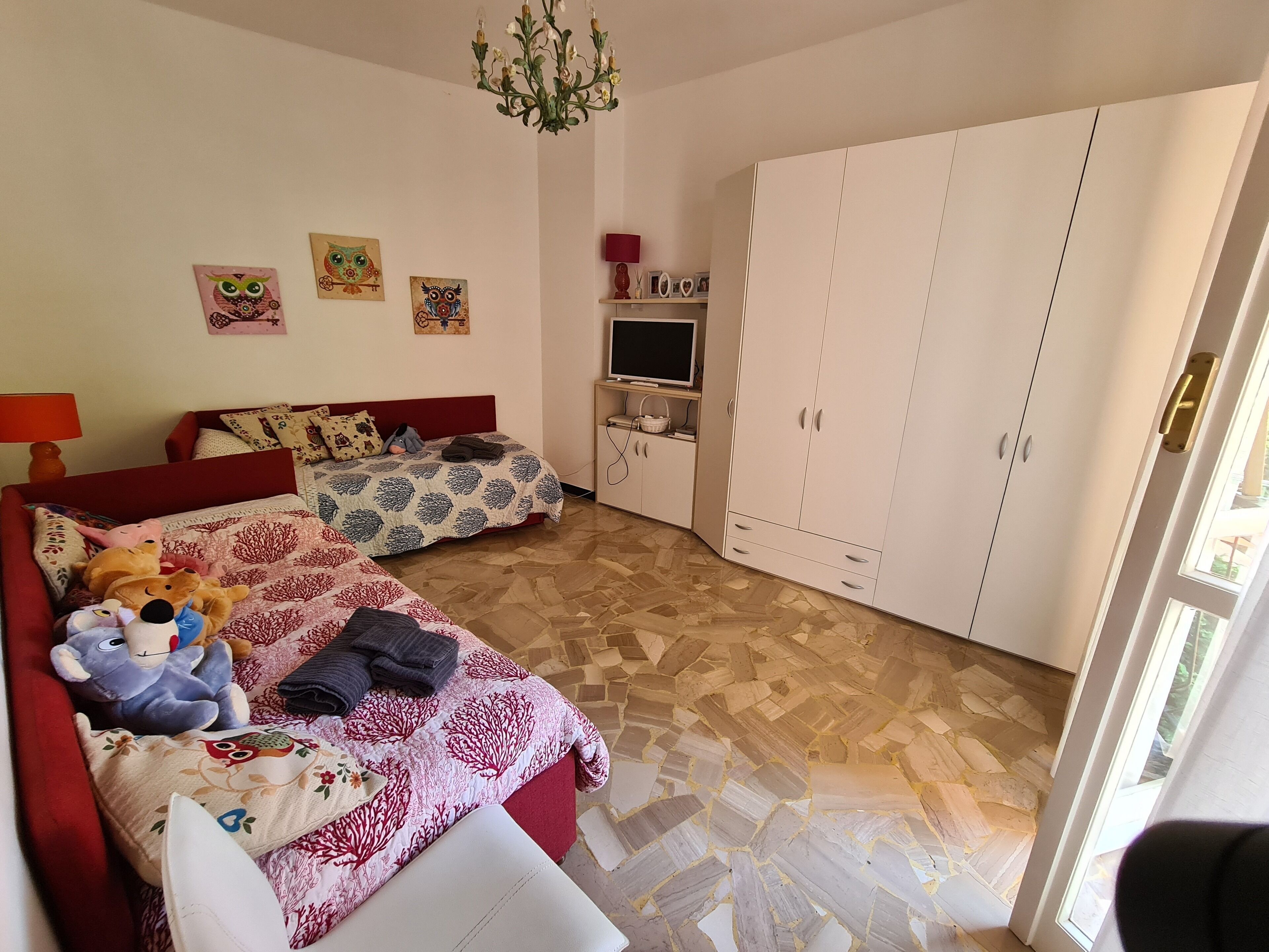 A bedroom with a bed, a TV, a wardrobe, and a chandelier.