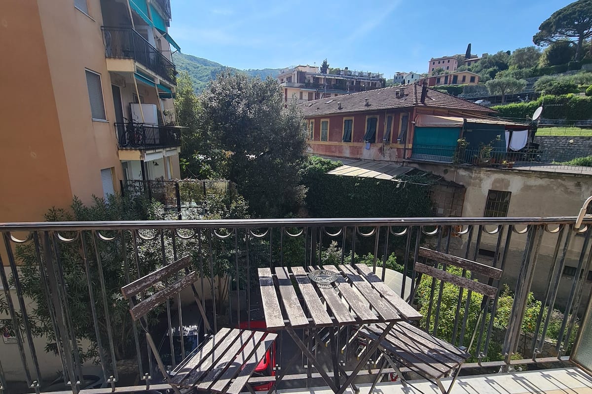 Ein Balkon mit Metallgeländer, einem Holztisch und Blick auf umliegende Gebäude und Grünflächen.