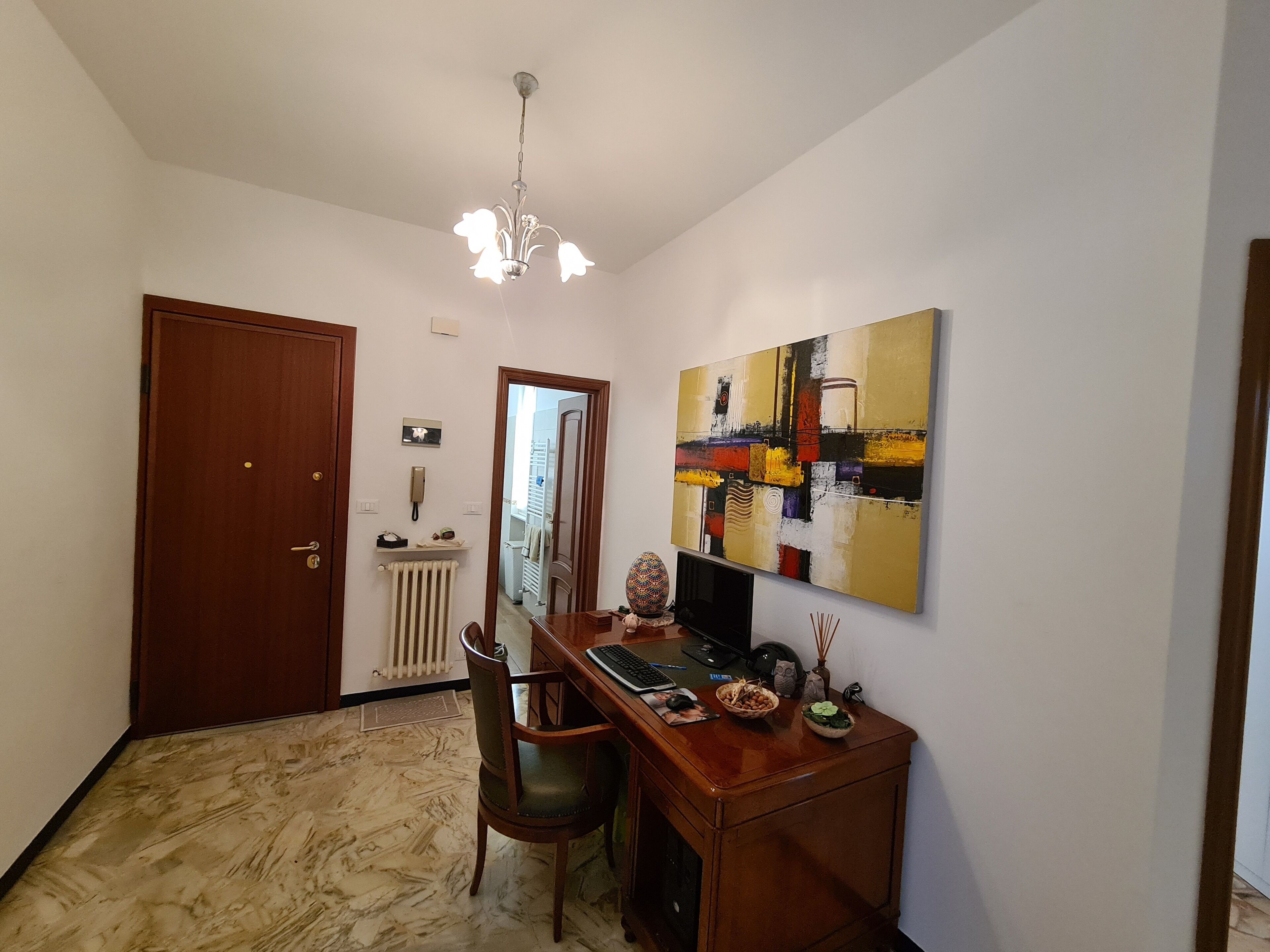 Quarto com escrivaninha de madeira, cadeira e uma grande pintura abstrata na parede.