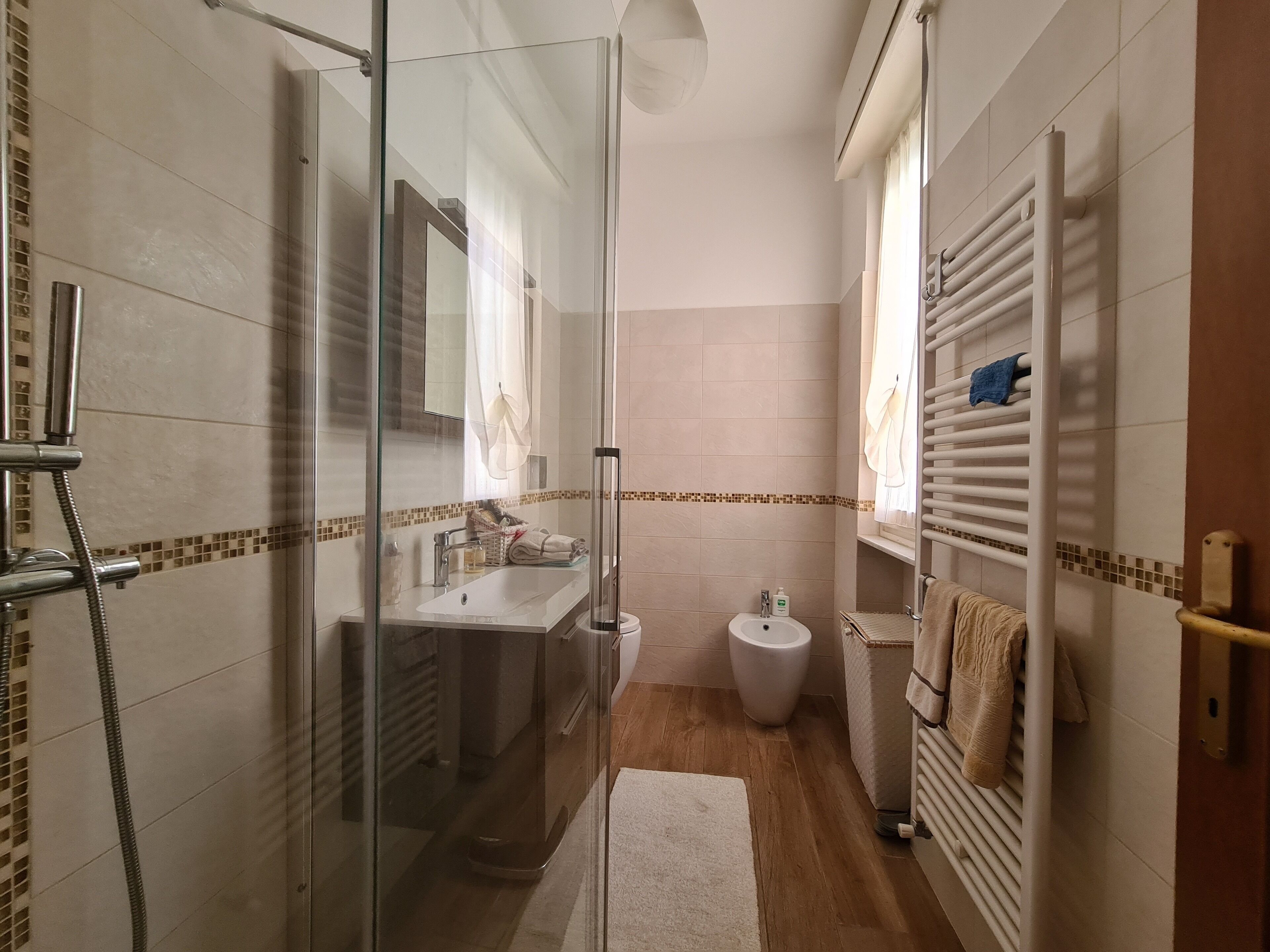 Uma casa de banho moderna com cabine de duche em vidro, lavatório com espelho, sanita e porta-toalhas.