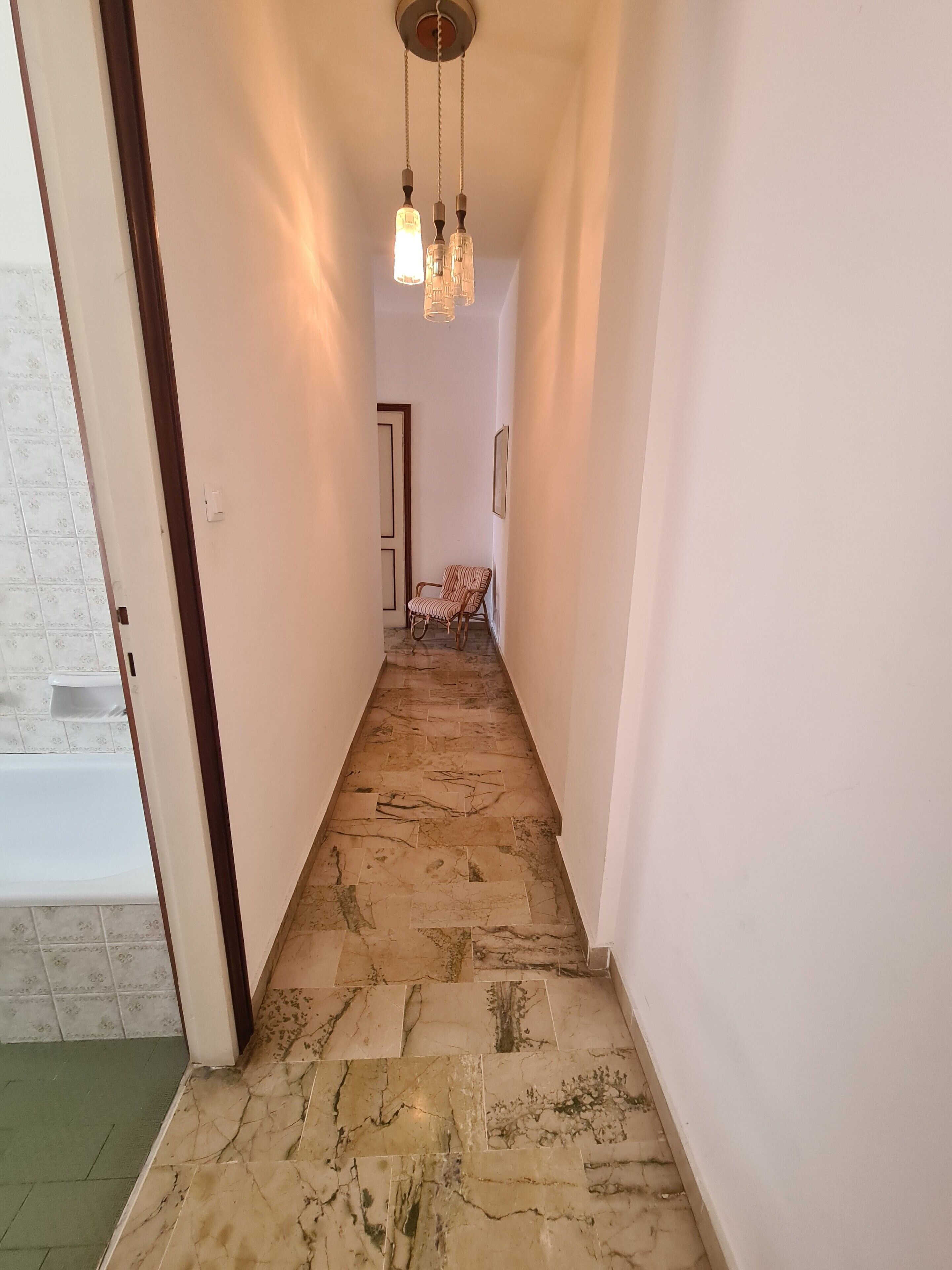 Un couloir étroit doté d’un sol à motifs, d’une chaise et d’un luminaire suspendu.