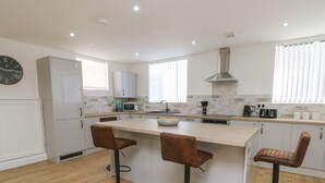 A modern kitchen with a central island, two bar stools, a microwave, and a toaster. - The Church (Holyhead)