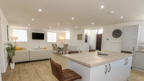 A modern kitchen with a central island, white cabinetry, and a dining area with a round table and chairs. - The Church (Holyhead)