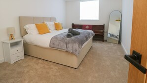 A bedroom with a bed, bedside table, lamp, and a window. - The Church (Holyhead)