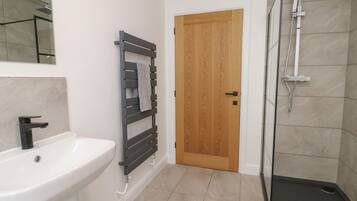 Un baño con lavamanos blanco, toallero, puerta de madera y cabina de ducha de vidrio.