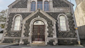 A historic building with a prominent arched entrance, a clock tower, and a sign indicating it is the English Presbyterian Church from 1891. - The Church (Holyhead)