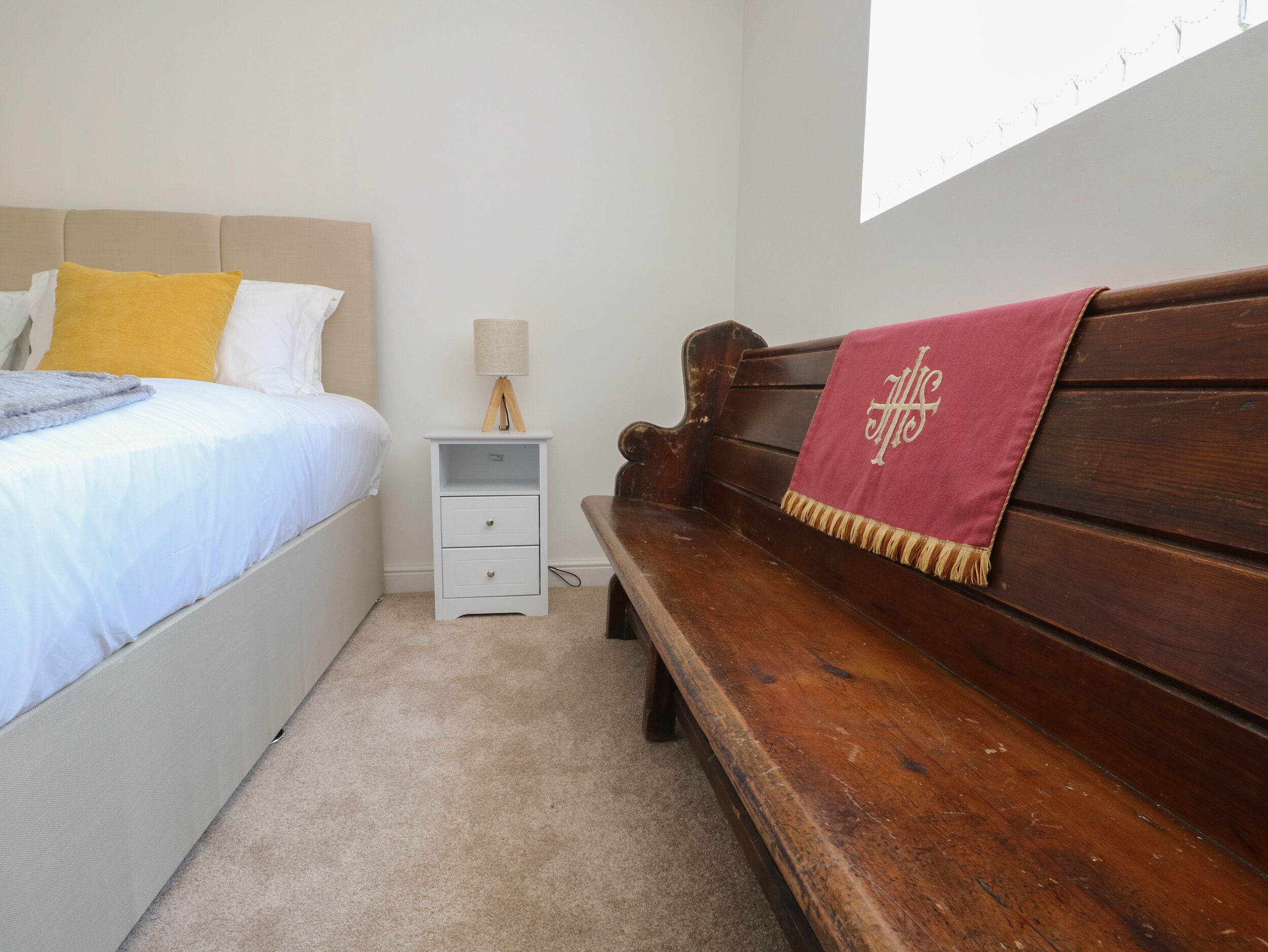 Une chambre à coucher comprenant un lit, une table de chevet, un banc en bois et une lampe fixée au mur.