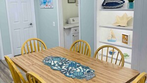 Uma área de refeições com mesa de madeira e cadeiras amarelas, uma porta branca e uma prateleira com objetos decorativos.